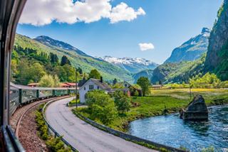 A scenic view of Flåm showcasing lush mountains, a winding river, and a picturesque train route | MSC Cruises