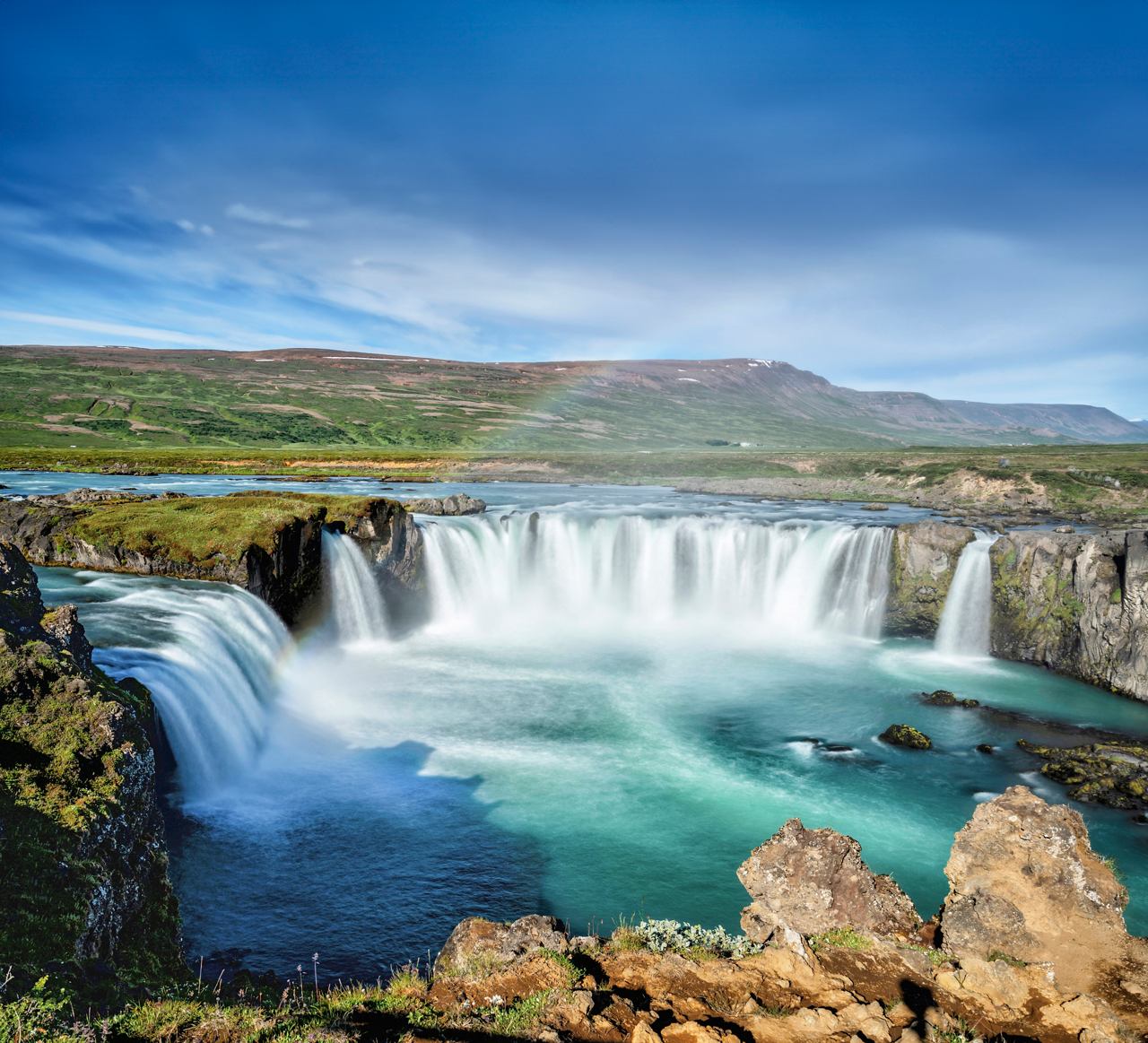 La cascada de Godafoss cae en una piscina turquesa rodeada de un paisaje exuberante y formaciones rocosas | MSC Cruceros