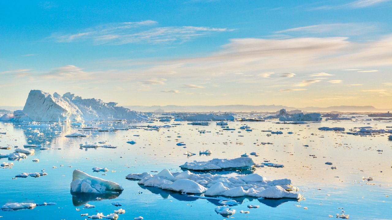 A serene view of icebergs floating in the tranquil sea under a beautiful sky in Greenland | MSC Cruises