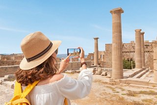 A woman in a hat captures a moment at the archaeological site of Rhodes, surrounded by ancient columns | MSC Cruises