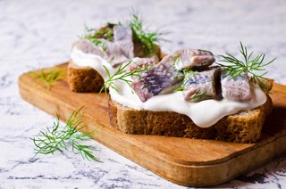 A beautifully arranged open sandwich topped with herring, cream, and herbs on a wooden board | MSC Cruises
