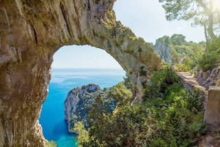 Una vista impresionante a través de un arco natural revela el vibrante mar azul y la exuberante costa de Capri | MSC Cruceros