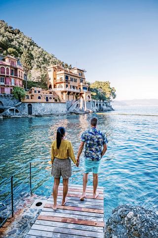 A couple stands on a pier overlooking the tranquil waters of Portofino, surrounded by charming coastal houses | MSC Cruises