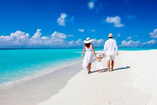Eine Familie spaziert Hand in Hand entlang eines sonnigen Strandes mit türkisfarbenem Wasser und blauem Himmel in der Karibik | MSC Cruises