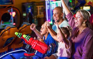A family enjoying a fun moment while playing arcade games together in an entertainment area | MSC Cruises