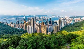 Vue panoramique de la skyline de Hong Kong avec une verdure luxuriante au premier plan et un ciel bleu clair au-dessus | MSC Cruises