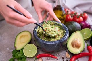 A hand prepares fresh guacamole with avocados and tomatoes, surrounded by vibrant ingredients | MSC Cruises