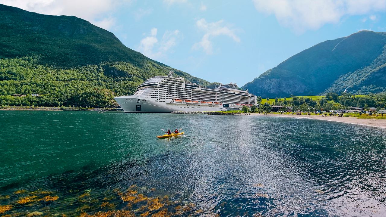 Ein atemberaubender Blick auf die MSC Grandiosa, die in einem ruhigen Fjord vor Anker liegt, umgeben von Bergen und blauem Himmel | MSC Cruises