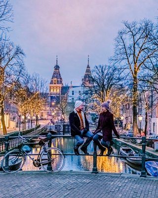 A couple enjoying a romantic evening stroll by a beautifully lit canal in Amsterdam during the festive season | MSC Cruises