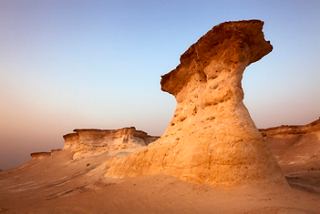 A striking limestone formation rises against a soft sunset sky in the Qatari desert | MSC Cruises