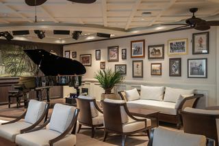 A warm sitting area with elegant decor, featuring a piano and tables for relaxation in the Raj Polo Tea House | MSC Cruises