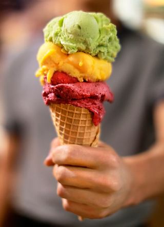A hand holding a colourful ice cream cone with three scoops of fruity flavours | MSC Cruises