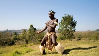 A person performs a traditional dance on a grassy landscape under a clear blue sky | MSC Cruises