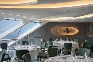 Elegant dining area in the MSC Yacht Club, featuring tables, chairs, and a stunning view of the sea through glass walls | MSC Cruises