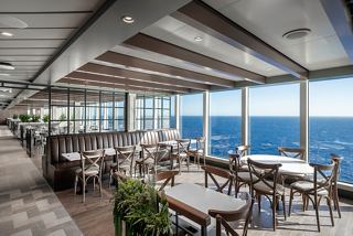 A bright restaurant with panoramic views of the ocean, featuring stylish tables and greenery | MSC Cruises
