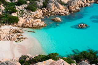 Turquoise waters gently lapping against a sandy beach surrounded by rocky formations in Cala Coticcio, Italy | MSC Cruises