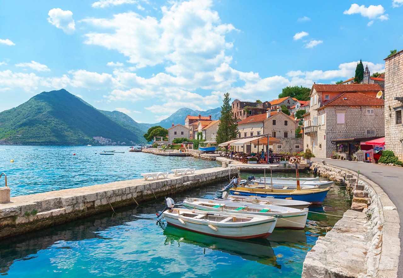 A serene view of Kotor Bay with boats and charming buildings under a bright summer sky | MSC Cruises