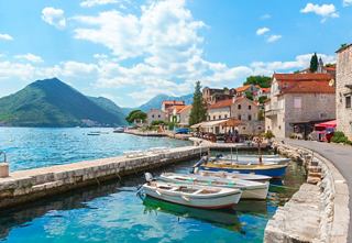 A serene view of Kotor Bay with boats and charming buildings under a bright summer sky | MSC Cruises