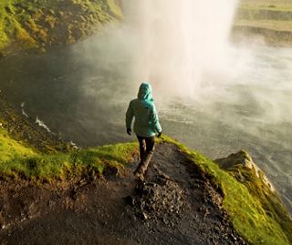 A woman in a jacket strolls by a waterfall in Iceland | MSC Cruises