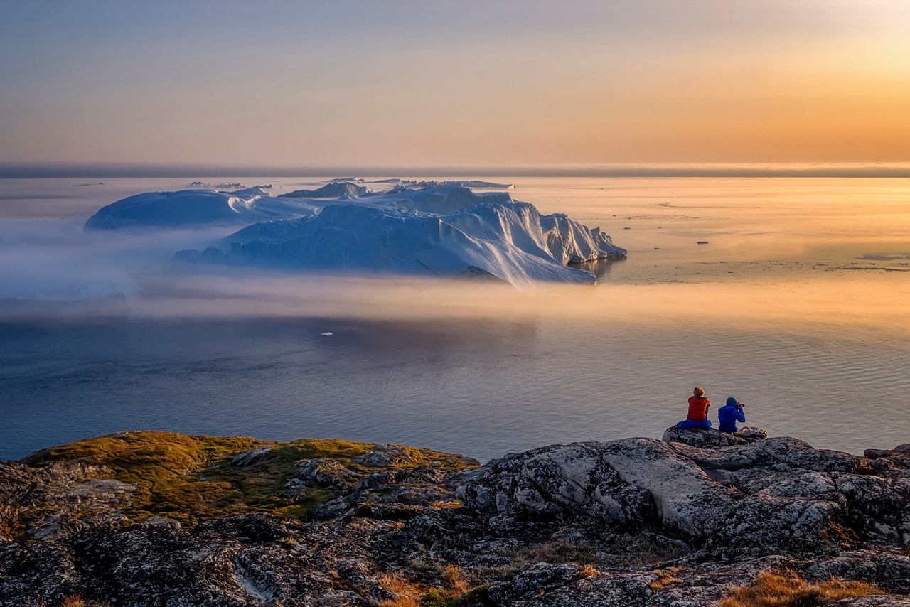 Two people enjoy a scenic sunset view over the sea and an iceberg in Ilulissat, Greenland | MSC Cruises