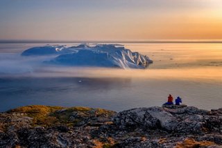 Two people enjoy a scenic sunset view over the sea and an iceberg in Ilulissat, Greenland | MSC Cruises