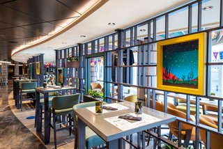 A vibrant dining area in Hola! Tacos & Cantina featuring tables, footstools and colourful artwork | MSC Cruises