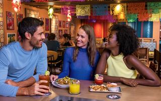 Three friends enjoying drinks and laughter at a vibrant Latin American restaurant aboard MSC World Europa | MSC Cruises