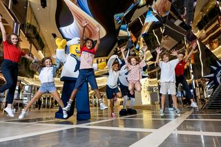 Children joyfully participate in a lively kids' parade with mascots and entertainers in the vibrant World Galleria | MSC Cruises