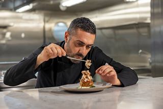 Un chef está emplatando cuidadosamente un plato gourmet con pinzas en la cocina del MSC World Europa | MSC Cruceros