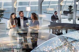 Friends enjoying cocktails in the Top Sail Lounge aboard MSC World Europa, with a musician playing in the background | MSC Cruises