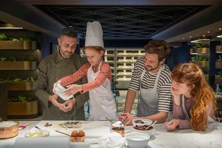 Una familia participa en una clase de cocina, aprendiendo a hacer galletas con un chef en un ambiente cálido | MSC Cruceros
