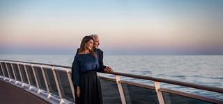 Una mujer disfruta de un momento sereno junto al mar al atardecer, apoyada en la barandilla del MSC World Europa | MSC Cruceros