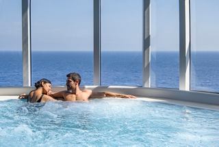 Una pareja se relaja junta en un jacuzzi, disfrutando de impresionantes vistas al mar a través de una pared de vidrio | MSC Cruceros