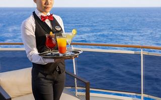 A waiter presents a colourful cocktail while standing on the deck, with the sea and sky in the background | MSC Cruises