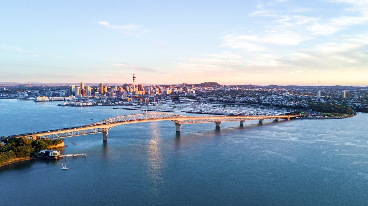 A stunning aerial view of Auckland Harbour showcasing the iconic bridge and skyline reflecting in the sea | MSC Cruises