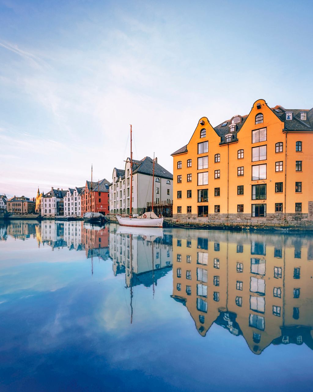 Des maisons colorées au bord de l'eau se reflètent dans la mer calme d'Ålesund, en Norvège, créant une atmosphère sereine | MSC Cruises