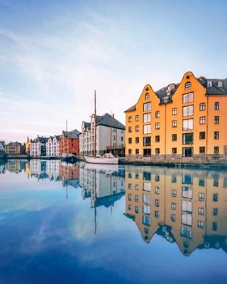 Colourful waterfront houses reflect in the calm sea of Ålesund, Norway, creating a serene atmosphere | MSC Cruises