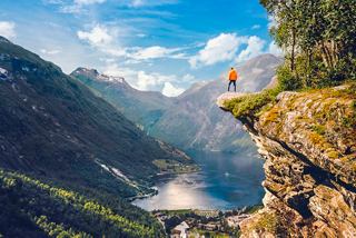 A lone hiker stands on a cliff, overlooking the stunning Geirangerfjord and majestic mountains in Norway | MSC Cruises