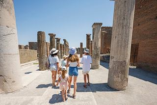 A family explores the ancient ruins of Pompeii, surrounded by historic columns under a clear blue sky | MSC Cruises