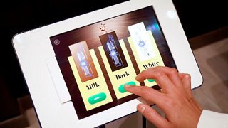 A hand interacting with a tablet displaying options for selecting chocolate bars at Jean-Philippe Chocolat & Café | MSC Cruises