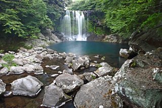 Una vista serena delle cascate Cheonjeyeon che si riversano in uno stagno tranquillo circondato da vegetazione lussureggiante e rocce | MSC Crociere