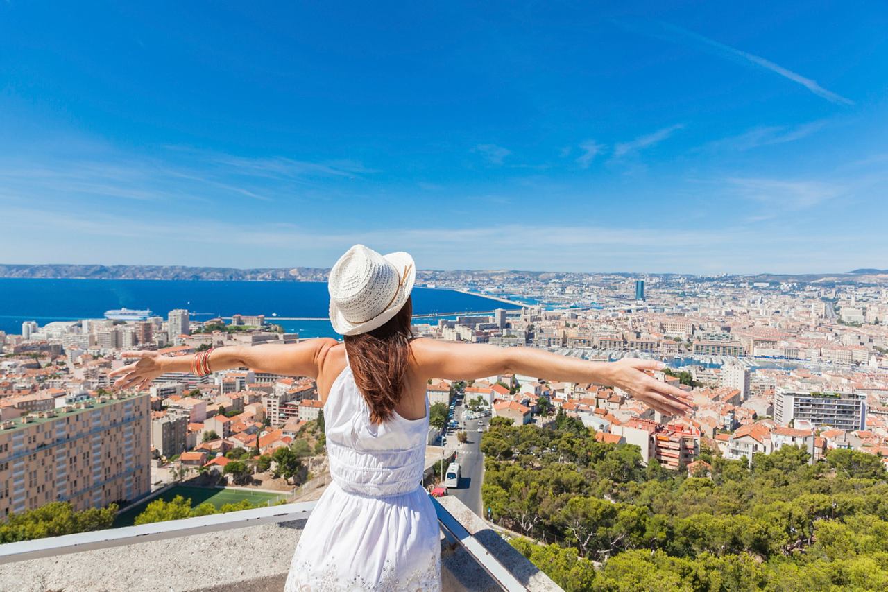 A woman in a white dress stands with arms outstretched, enjoying the panoramic view of Marseille and the Mediterranean Sea | MSC Cruises