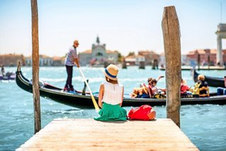 A woman sits at a dock in Venice, enjoying the view of a gondola and the vibrant canal scene | MSC Cruises