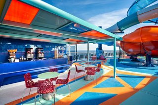 Gäste genießen erfrischende Getränke an der lebhaften Ocean Cay Bar mit einer Wasserrutsche im Hintergrund | MSC Cruises