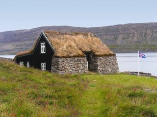 A rustic house with a thatched roof overlooks a serene fjord in Iceland's stunning landscape | MSC Cruises