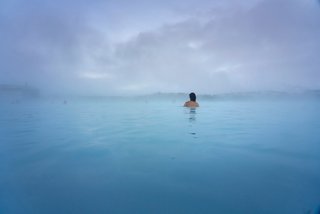 A serene landscape features a solitary figure in the tranquil waters of Iceland's Blue Lagoon | MSC Cruises