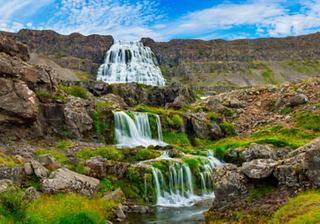 A stunning waterfall cascades down rocky terrain, surrounded by lush green vegetation under a bright blue sky | MSC Cruises