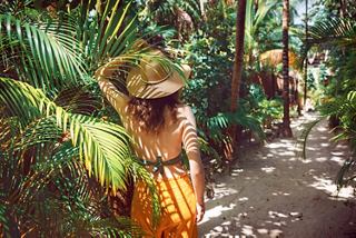 A woman in a summer outfit strolls along a lush path surrounded by palm trees in Cozumel | MSC Cruises