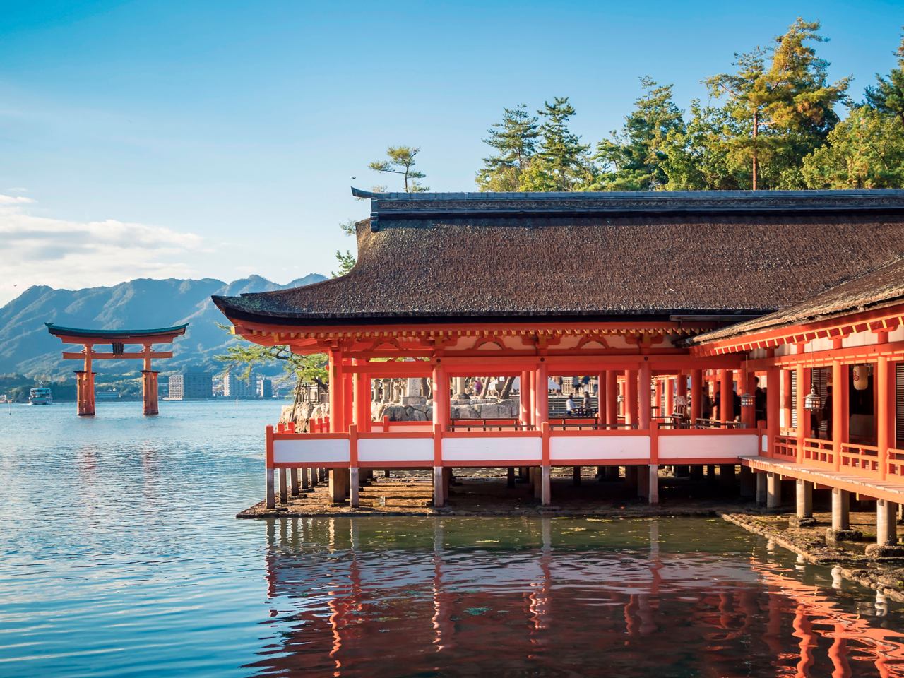 A serene view of a traditional Japanese structure by the water, framed by lush greenery and a distant Torii gate | MSC Cruises