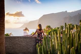 Eine Frau genießt die ruhige Aussicht auf die Atlantikküste und die Berge von Teneriffa, umgeben von Kakteen | MSC Cruises